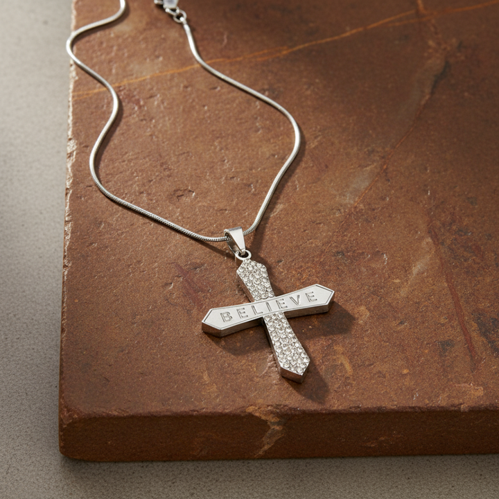Silver cross pendant with 'BELIEVE' engraving on a stone surface